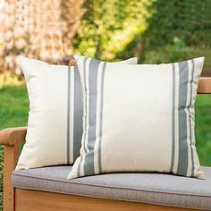 two pillows sitting on top of a wooden chair in front of a green grass covered field