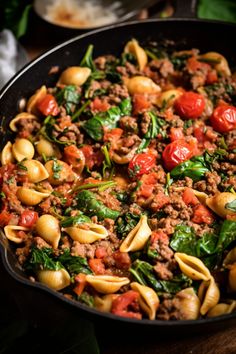 a skillet filled with pasta and spinach covered in ground beef, tomato sauce