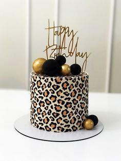 a leopard print birthday cake with gold and black decorations on the top, sitting on a white table