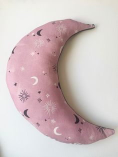 a pink crescent pillow with stars and moon designs on the front, sitting against a white wall