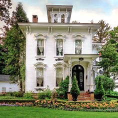 a large white house with lots of flowers in the front yard and landscaping around it