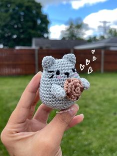 a hand holding a tiny crocheted cat with a donut in it's mouth