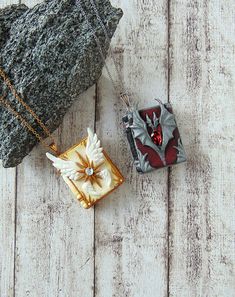 two pieces of jewelry sitting next to each other on a wooden surface, one with an ornament in the shape of a bird