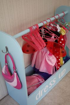 a child's dress up storage unit with pink and blue clothes hanging on it