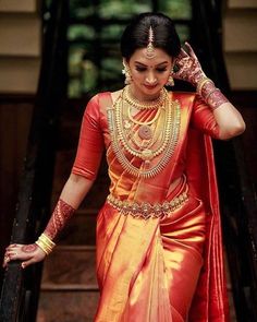 a woman in an orange and yellow sari walking down stairs with her hands on her head