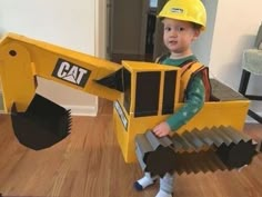 a young boy wearing a construction themed costume and holding a large toy bulldozer