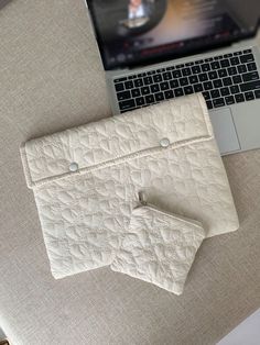 an open laptop computer sitting on top of a table next to a quilted purse