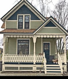 a house that is painted green and has white railings on the front porch, and blue trim around the windows