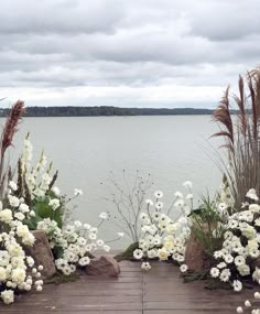 some white flowers and plants on a wooden platform by the water with clouds in the sky