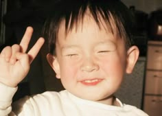 a young boy making the peace sign with his fingers in front of him and wearing a white shirt