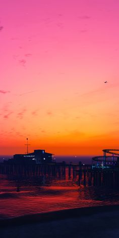 the sky is pink and orange as the sun sets over the ocean with a pier in the distance