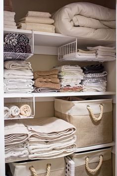 an organized closet with linens, blankets and other items in white baskets on shelves