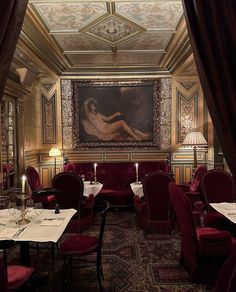 a dining room with red velvet chairs and tables in front of a painting on the wall