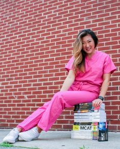 a woman sitting on top of a stack of books in front of a brick wall