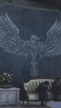 two people sitting on a couch in front of a wall with an eagle painted on it