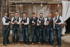 a group of men standing next to each other holding puppies in their hands and wearing vests