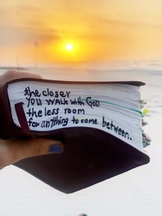 someone is holding up a book with the sun setting in the background and writing on it