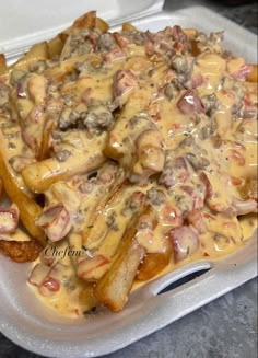 a container filled with french fries covered in gravy and toppings on top