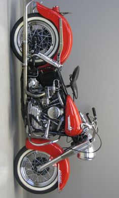 a red motorcycle parked on top of a white wall next to a metal rack with two motorcycles