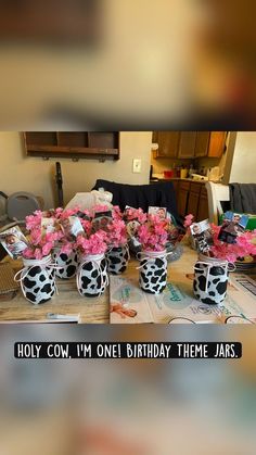 a table topped with black and white vases filled with pink flowers on top of a wooden table