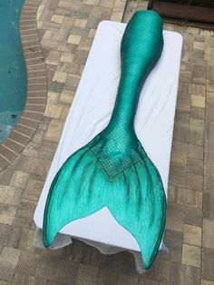 a large green mermaid tail laying on top of a white sheet next to a swimming pool