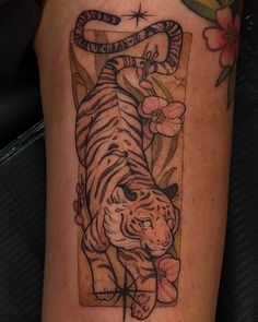 a tiger tattoo on the leg of a woman's arm with flowers and leaves