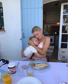 a woman holding a baby while sitting at a table with food and drinks on it