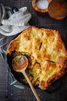 a pot pie with spinach and cheese in it on a wooden table next to two spoons