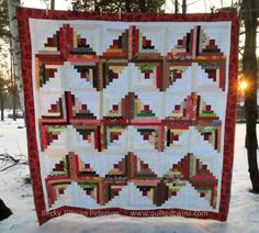 a quilt is hanging from a tree in the snow with it's red border