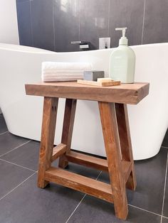 a wooden table sitting in front of a bath tub next to a white towel and soap dispenser