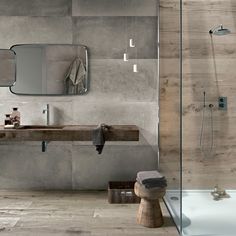 an instagramted photo of a bathroom with grey walls and wood accents, including a large mirror over the bathtub