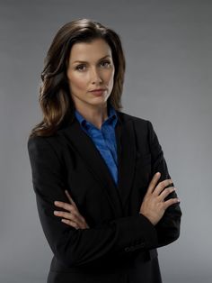 a woman with her arms crossed wearing a black suit and blue shirt is looking at the camera