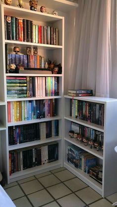 a book shelf filled with lots of books next to a white chair and window in a room