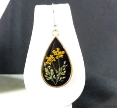 a pair of earrings with yellow flowers on them sitting on a white display stand in front of a black background