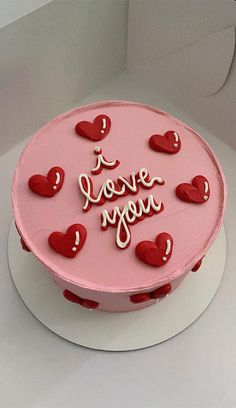 a pink cake decorated with hearts and the words i love you on it's side