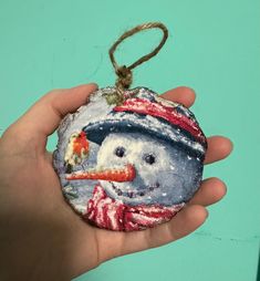 a hand holding an ornament with a snowman on it's face