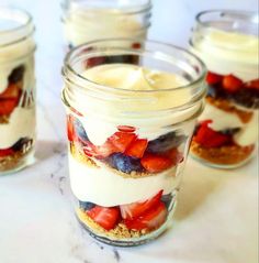 four mason jars filled with desserts on top of a white tablecloth covered in blueberries, strawberries and cream