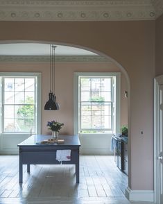 an archway leads to the kitchen and dining area in this home with pink walls, hardwood floors, and black pendant lights