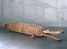 a wooden alligator with teeth and spikes on it's back, sitting in front of a concrete wall