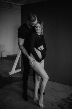 black and white photograph of a pregnant woman hugging her husband's belly in an empty room