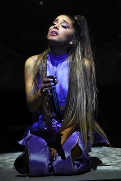 a woman with long hair sitting on the ground holding a microphone in her hand and looking up