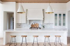 a kitchen with white cabinets and wooden stools in front of an island that has four bar stools on it