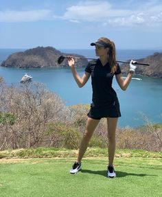 a woman standing on top of a lush green field next to a golf ball and club