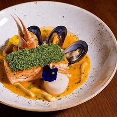 a white bowl filled with seafood and mussels on top of a wooden table