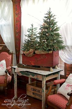 a christmas tree in a wooden box on top of a table next to two chairs