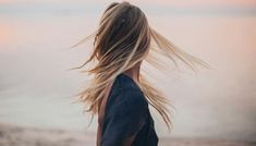 a woman standing on the beach with her hair blowing in the wind and looking at the ocean