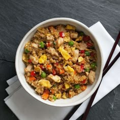 a white bowl filled with food next to chopsticks on top of a table