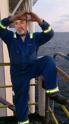 a man in blue overalls sitting on the side of a boat with his hands behind his head