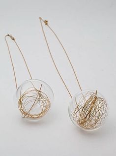 two clear glass vases with gold wire hanging from the sides on a white surface