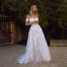 a woman in a white wedding dress standing on the ground with her arms crossed and looking up